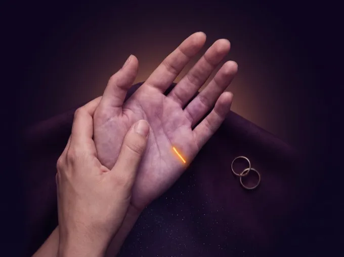 Two hands held together beside a pair of wedding rings